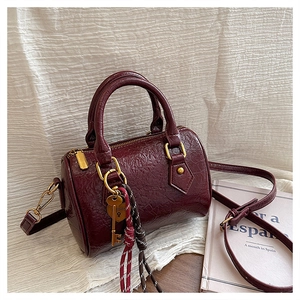 Detailed close-up of wine red Boston bag with shiny gold hardware and heart pendant