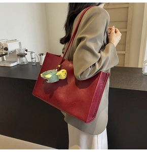 Detailed view of red retro leather tote bag featuring a green plush turtle charm