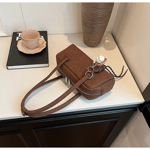 Detail of a brown matte leather shoulder bag with side embossing and baseball charm