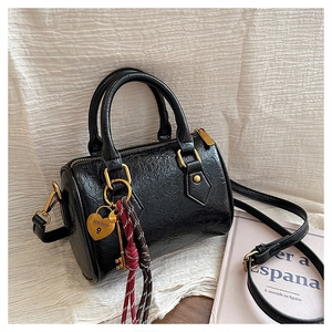 Detail of black Boston bag with gold heart lock, woven charm and pleated leather texture