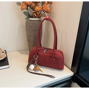 Detail of dark red suede underarm bag featuring baseball themed charms and logo embossing