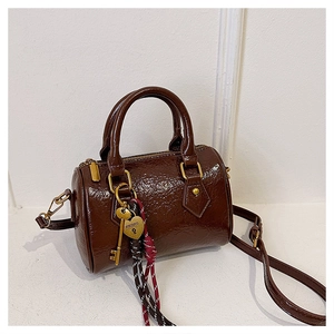 Detail showing brown glossy Boston bag with golden heart padlock and woven rope charms