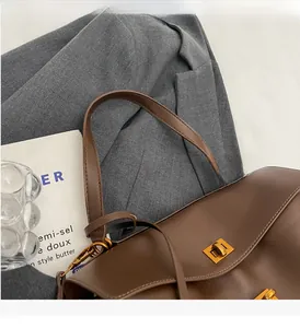 Close-up of brown leather tote bag with gold rotary buckle on grey blazer background