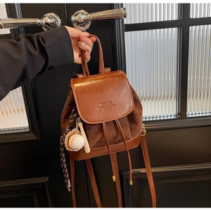 Detail of a brown leather and suede mini backpack featuring a baseball bat keychain