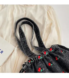 Close-up of black denim tote bag with red cherry embroidery and pleated opening detail