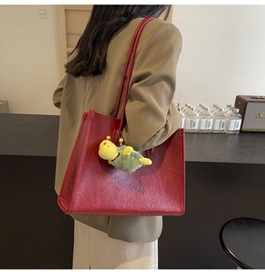 Detail of red tote bag with a small turtle plush charm on a long shoulder strap