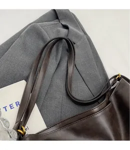 Detailed close-up of dark brown faux leather bag with long straps and gold metal rings