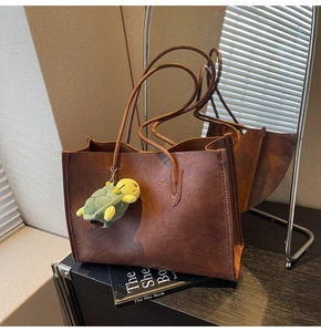 Close-up of brown vintage leather tote bag featuring a cute green turtle plush pendant