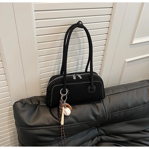 Close-up of black leather underarm bag with contrast stitching and baseball bag charm