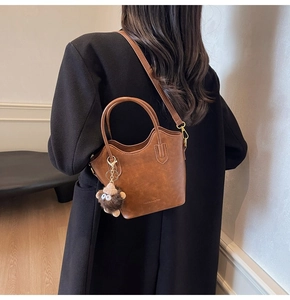 Dettaglio della borsa a secchiello vintage marrone con ciondolo in peluche e logo Fashion & YM
