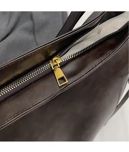 Close-up of golden metal zipper and dark brown leather texture on a vintage tote bag