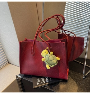 Detail of dark red faux leather tote bag with a green turtle plush charm decoration
