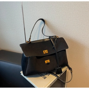 Detail of black tote bag with dual gold metal turn-locks and leather shoulder strap