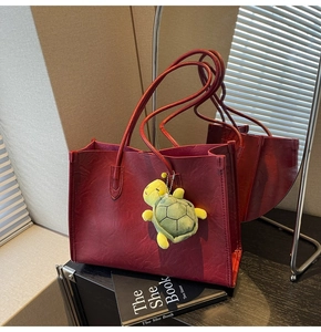 Detail of dark red tote bag with leather texture and a cute green turtle charm