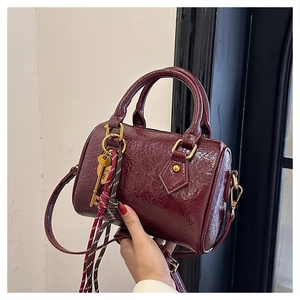 Detail of burgundy oil wax leather boston bag featuring gold hardware and heart key charm