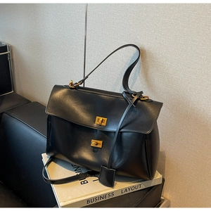 Close-up of black leather tote bag with dual gold twist locks on white business book