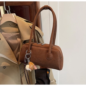Close-up of deep brown suede handbag featuring unique baseball charms and MUHETI branding