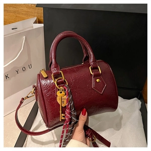 Detail of burgundy Boston bag with pleated texture and golden heart lock pendant