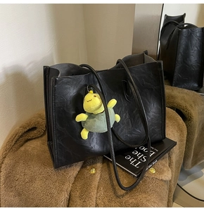 Close-up of black textured leather tote bag with a cute turtle plush charm