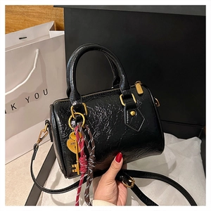 Close-up of black glossy Boston bag with gold hardware and woven rope charms in gift box