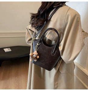 Dettaglio borsa a secchiello marrone vintage con ciondolo su modella in trench beige