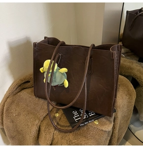 Detail of dark brown tote bag with natural leather texture and a cute turtle plush charm