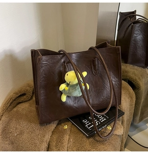 Close-up of deep brown leather tote with wrinkled texture and a cute turtle plush charm