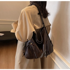 Detail of dark brown tote bag with zipper and leather bow on soft beige trench coat