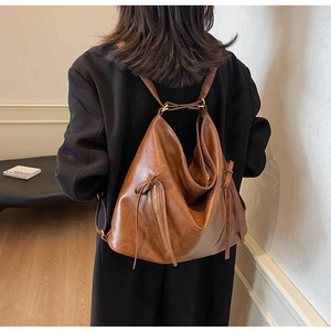 Detailed view of vintage brown leather backpack with tassel charms and metal dual zippers