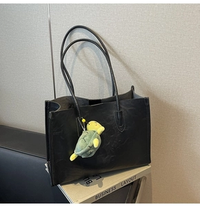 Close-up of black textured leather tote bag featuring a green turtle plush charm accessory