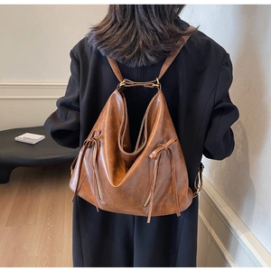 Detail view of vintage brown leather backpack showing dual side zippers and bow drawstring