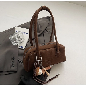 Close-up of brown suede shoulder bag featuring a stylish baseball and bat charm accessory
