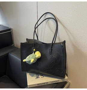 Detail of black tote bag with wrinkled texture and a green turtle plush charm on a book
