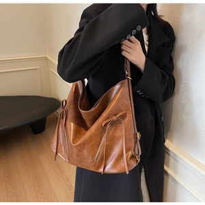 Caramel brown vintage tote bag with bow detail shown on a model in a minimal interior
