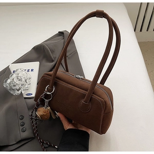 Detailed close-up of brown suede cylinder bag with white stitching and baseball glove charm