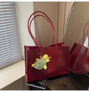 Detail view of red faux leather tote bag with crinkle texture and green turtle pendant
