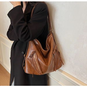 Detail of a brown leather tote bag showing decorative zippers and leather bow pendants