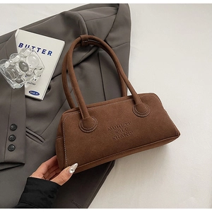 Detailed close-up of brown suede Boston bag with letter embossing in a minimalist setting