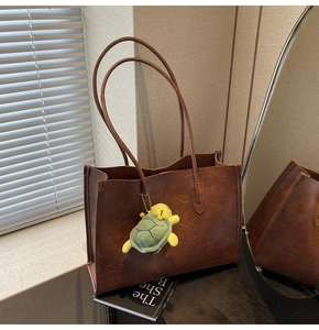 Detail of vintage brown tote bag with premium leather texture and turtle plush charm
