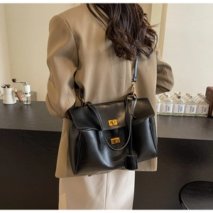 Detail view of black faux leather tote bag with gold metal twist locks in a cafe setting