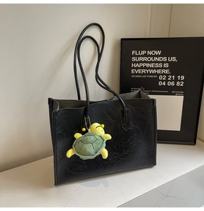 Detail of a large black vintage leather tote bag with a plush turtle charm on marble