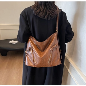 Close-up of a brown vintage tote bag with decorative zippers and a bow on a black coat