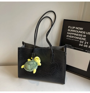 Detail of black tote bag with leather texture and cute green turtle plush charm accessory