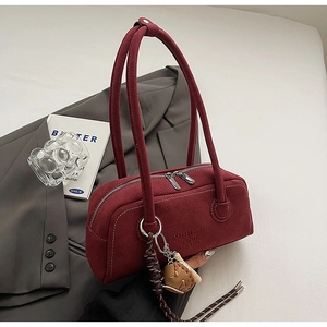 Detail of burgundy suede shoulder bag with dual zippers and woven doll pendant