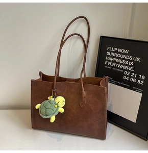 Close-up of a large dark brown faux leather tote bag with a cute green turtle charm