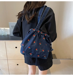 Detail view of denim bucket bag with red cherry embroidery and drawstring closure