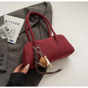 Detail of burgundy suede handbag with embossed logo and baseball themed bag charms