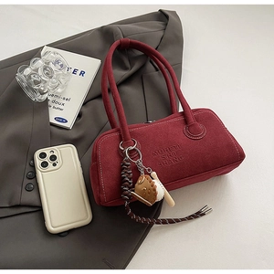 Detail of burgundy suede shoulder bag with MUHETI embossing on a gray blazer