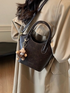 Secchiello vintage marrone scuro con ciondolo in peluche, abbinato a un trench coat