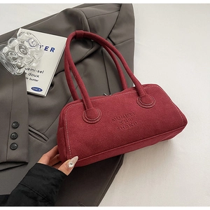 Detail of burgundy underarm bag with contrast stitching and embossed text on matte suede